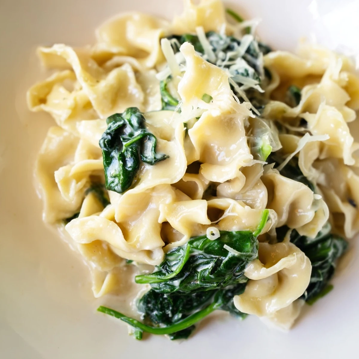 A close-up photo of creamy spinach garlic noodles twirling around a fork, with wilted green spinach leaves clinging to tender egg noodles in a rich, garlicky cream sauce.