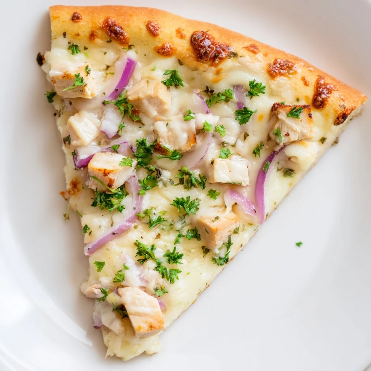 Close-up of Chicken Alfredo Pizza showing creamy white sauce, sliced red onions, and fresh parsley on a rustic board.