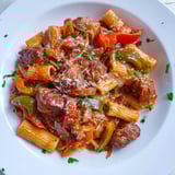 Close-up of golden-brown sausage and peppers pasta, garnished with fresh parsley and Parmesan.