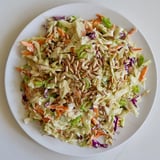 Close-up shot shows a bowl of homemade crunchy coleslaw salad beautifully topped with sunflower seeds.