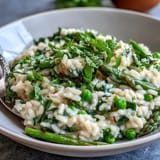 Creamy Spring Pea and Mint Risotto with Parmesan, topped with fresh herbs and lemon zest, perfect for an elegant vegetarian dinner party.
