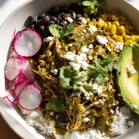 A close-up of a vibrant Green Enchiladas Rice Bowl overflowing with toppings, ready to eat.