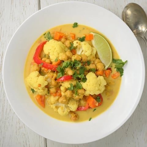 Steaming bowl of curried cauliflower and chickpea stew, garnished with fresh cilantro and lime wedges.