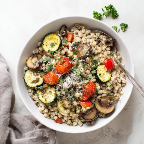 A warm bowl of Pearled Barley Creamy Bowl topped with colorful roasted zucchini, bell peppers, and cherry tomatoes garnished with fresh parsley.  