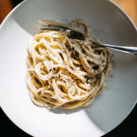 Steam rises from the freshly cooked spaghetti, tossed with grated Pecorino Romano and cracked black pepper.  