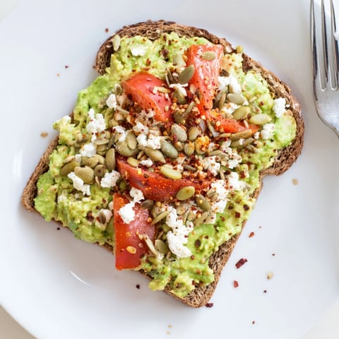 Creamy avocado mash on crisp, toasted whole grain bread, topped with fresh tomatoes and a sprinkle of seeds.