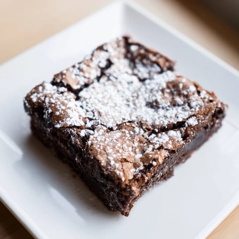 Close-up of freshly baked brownie squares, showing a soft, chocolatey interior, with powdered sugar.