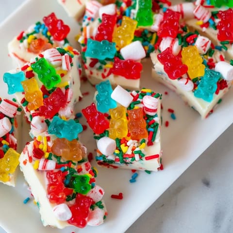 Gummy bears and candy canes adorn a rectangular slab of white chocolate, ready to be broken and enjoyed.