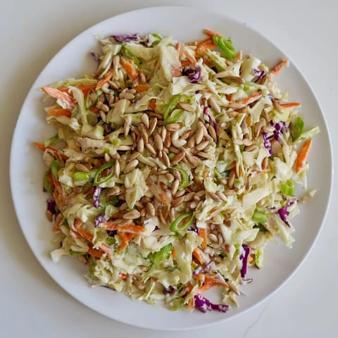 Close-up shot shows a bowl of homemade crunchy coleslaw salad beautifully topped with sunflower seeds.