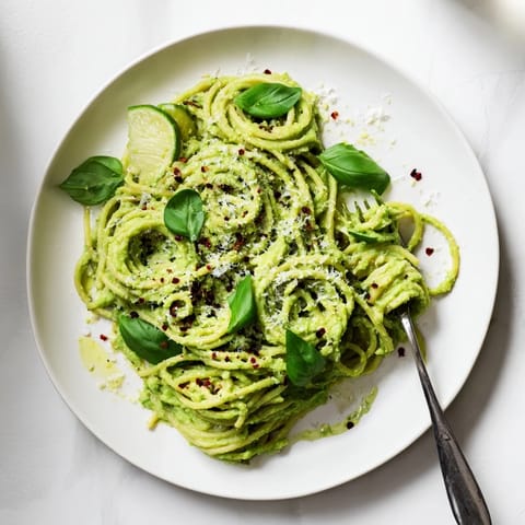 Creamy Smashed Avocado Pasta twirled on a fork, topped with fresh basil, lime wedges, and chili flakes for a vibrant, zesty meal.