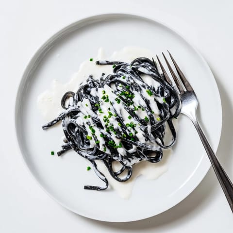 Creamy sauce clings to al dente Squid Ink Pasta, topped with chives and lemon wedges for a dramatic main dish.