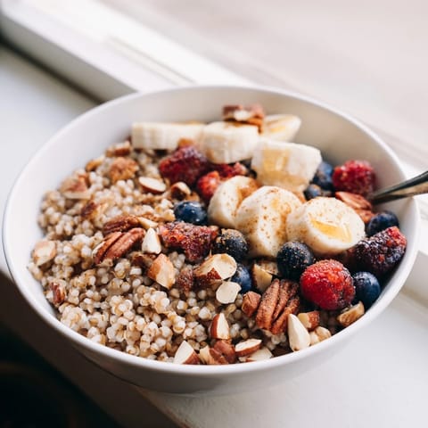 A warm bowl of Buckwheat Groats Breakfast topped with fresh berries, sliced banana, and chopped nuts, drizzled with honey.  