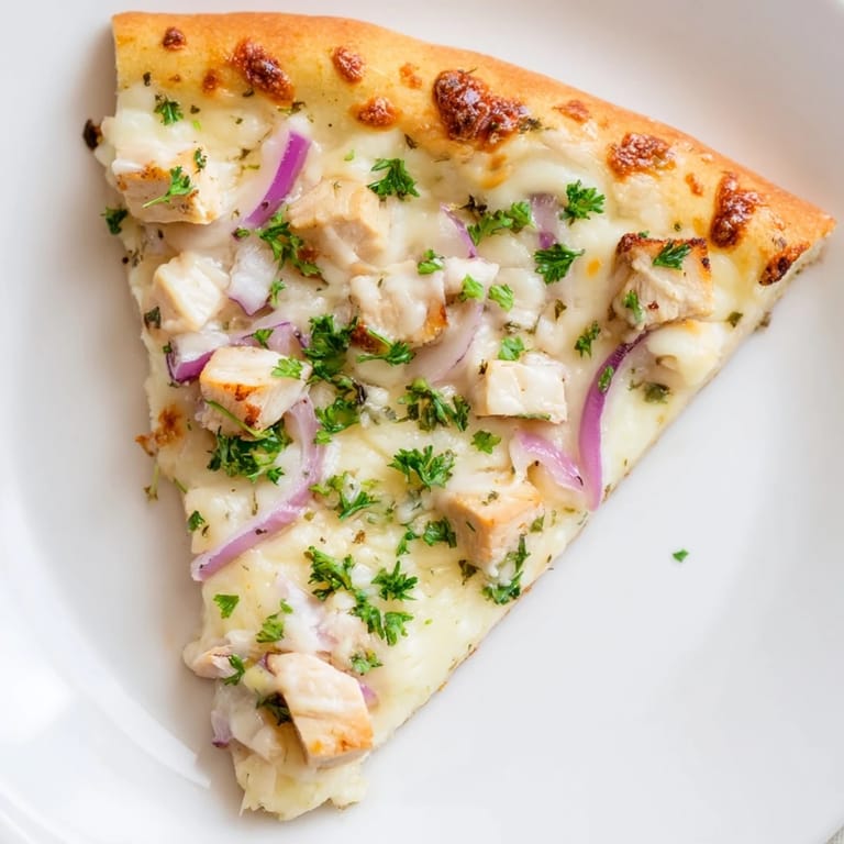Close-up of Chicken Alfredo Pizza showing creamy white sauce, sliced red onions, and fresh parsley on a rustic board.