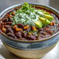 Hearty black bean and corn chili topped with tangy lime crema, garnished with fresh cilantro and avocado slices.  