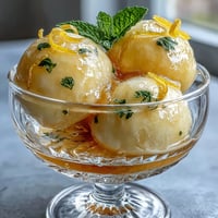 Vibrant limoncello sorbet in chilled glasses, garnished with fresh mint and lemon zest for a refreshing summer dessert.