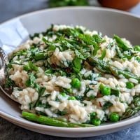 Creamy Spring Pea and Mint Risotto with Parmesan, topped with fresh herbs and lemon zest, perfect for an elegant vegetarian dinner party.